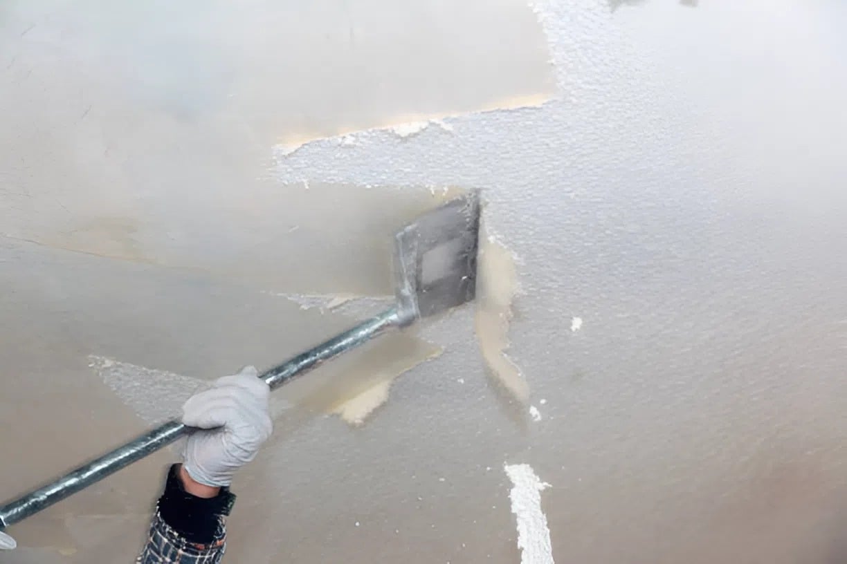 Professional painter in Richmond, VA, using a wide scraper to remove popcorn ceiling texture during a ceiling resurfacing project